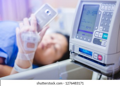 Selective Focus To Infusion Pumps With Blurry Patient Play Smart Phone In Hospital. The Concept Of Working Anytime.