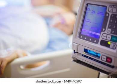 Selective Focus To Infusion Pumps With Blurry Patient In Hospital. Blurry Female Patients Lying In The Nursing Bed.