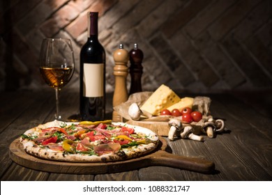 Selective Focus Of Italian Pizza, Spices, Cheese, Cherry Tomatoes And Bottle Of Wine On Wooden Surface