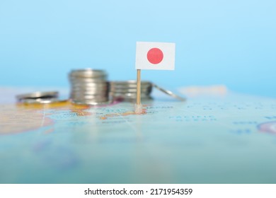 Selective Focus Of Japanese Flag In Blurry World Map With Coins. Japan Economy And Wealth Concept.	