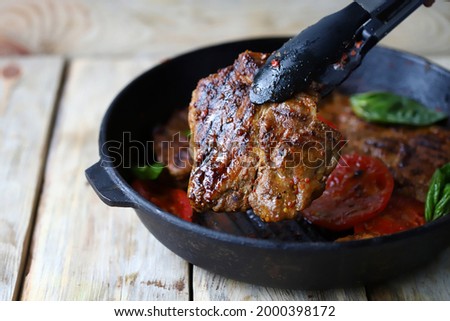 Selective focus. Juicy appetizing grilled steak. Tongs for meat and a frying pan with steaks.