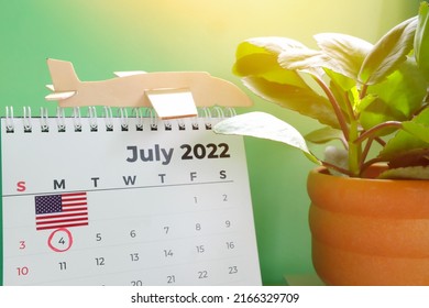 Selective focus of July 2022 desk calendar with marked date 4th of July, flag and airplane model. United States Independence day celebration and holiday travel concept.