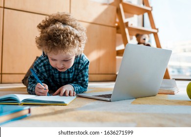 Selective Focus Of Kid Listening Music In Wireless Headphones While Writing Near Laptop