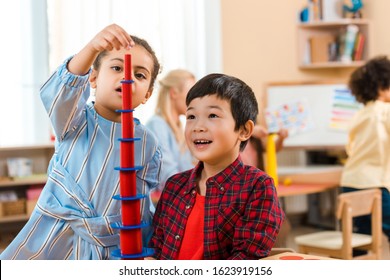 Selective Focus Of Kids Playing Educational Game With Teacher And Child At Background In Montessori Class