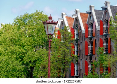 Selective focus of lamp pole in Amsterdam in spring with blurred view of architecture traditional canal houses, Old warehouse with red windows (Pakhuis) at Prinsengracht as background, Netherlands.
