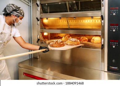 Selective Focus Of Latino Baker Putting Bread In The Oven With Gloves And A Mask Due To The 2020 Covid19 Coronavirus Pandemic