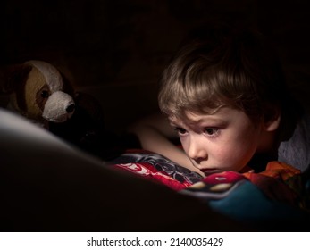 Selective Focus. Little Boy Sitting In The Dark And Watching Cartoons On Mobile. Light Reflection On Kid Face From Phone.