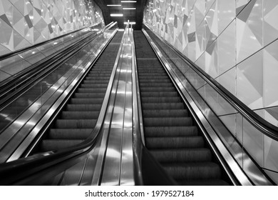 Selective focus and low angle view, black and white tone, interior view of stairway over handrail of escalator from underground metro station without people.