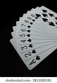 A selective focus macro shot of black spades suit playing cards from Ace to Ten arranged diagonally on a pitch-black background.