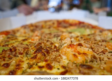 Selective focus and macro view at shrimp and tuna on top of seafood pizza and defocus background of white table and group of people.