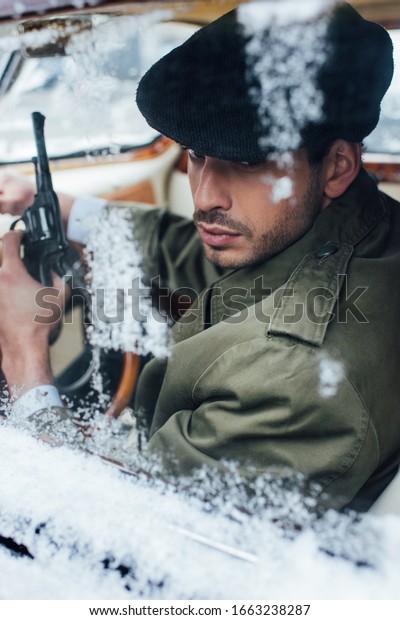 Selective focus of mafioso with gun in car covered\
with snow