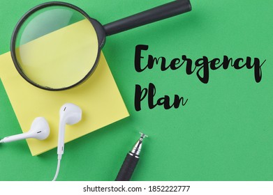 Selective Focus Of Magnifying Glass, Memo Note, Earphones And Pen Over A Green Bckground Written With Text EMERGENCY PLAN. 