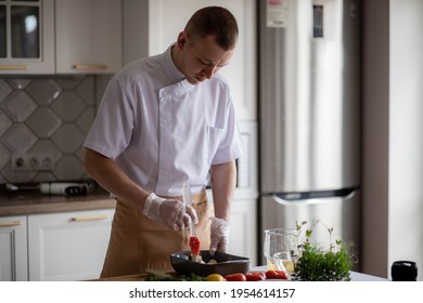 Selective Focus. Male Chef, Handsome Young Man, Preparing Healthy Food At Home With Ingredients For Cooking Healthy Food, Salad Of Tomato, Eggplant, Onion, Microgreen Peas And Sunflower. 