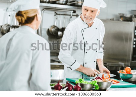 selective focus of male and female chefs in uniform looking at each other while cooking food in restaurant kitchen