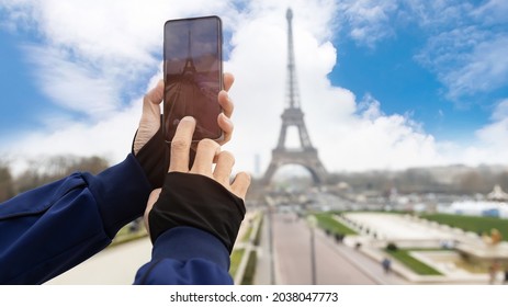 Selective focus of man hand with he is using smartphone take picture at View of Eiffel Tower with blue sky background in  Paris, France