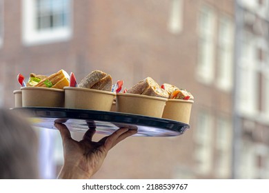 Selective Focus Of A Man Hand Holding A Tray Full With Sandwiches, Waiter Bringing The Food In Outdoor Banquet Cocktail Party, Close Up A Hand Of Server Serving The Sandwich In Resturant.