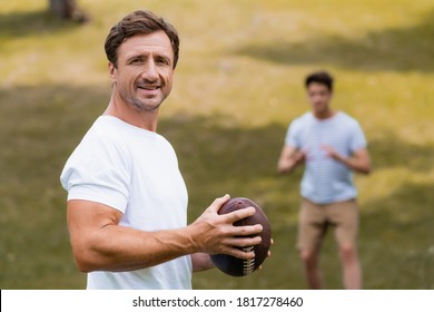 selective focus of man holding rugby ball and looking at camera near teenager son in green park - Powered by Shutterstock