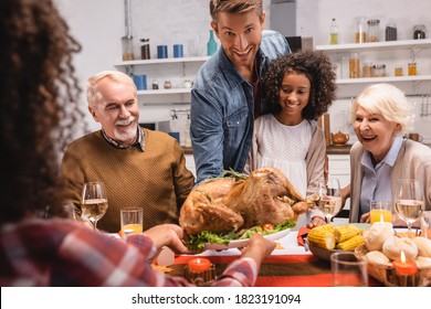 Selective Focus Of Man Looking At Camera Near Multiethnic Family And Thanksgiving Dinner With Decor On Table