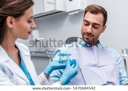 selective focus of man looking at teeth model in hands of attractive dentist