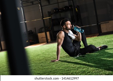 selective focus of man in sportswear drinking water while sitting on grass 