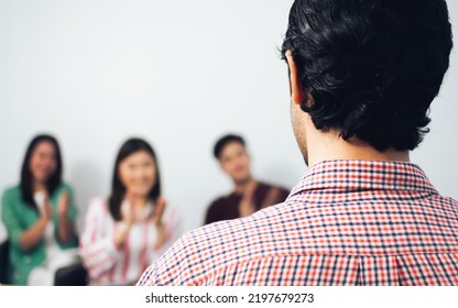 Selective Focus Of Man's Back While Teaching, Training Or Coaching People In A Room With Blur Background Of Happy Persons Clapping Their Hands. Seminar, Work Shop And Meeting Concept