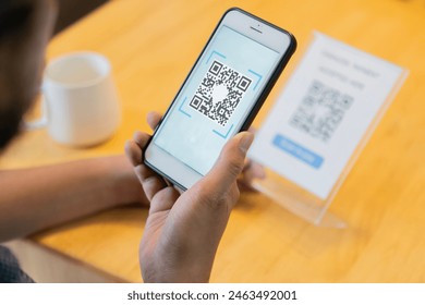 Selective focus of man's hand scanning QR code through mobile phone at cafe table. Qr code payment, E wallet , cashless technology concept. - Powered by Shutterstock