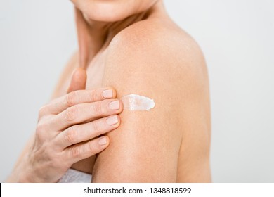 selective focus of mature woman applying cosmetic cream isolated on grey 