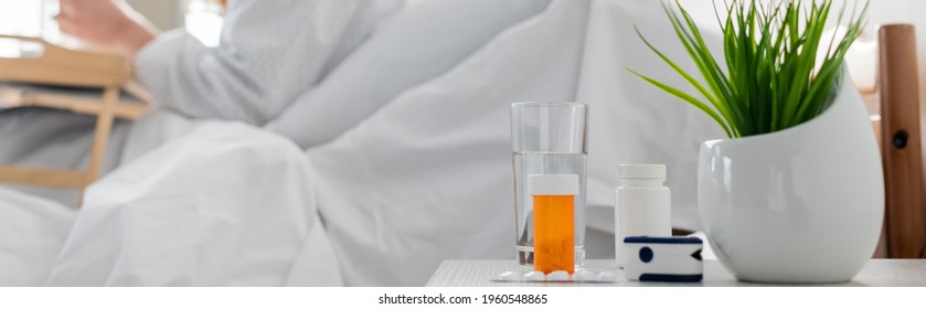 Selective Focus Of Medications, Pulse Oximeter, Plant And Glass Of Water Near Patient On Blurred Background, Banner