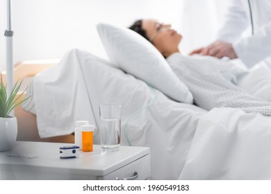 Selective Focus Of Medications, Pulse Oximeter And Glass Of Water Near Ill African American Woman And Doctor