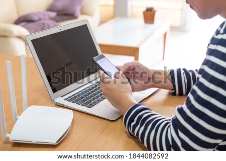 Selective focus at men hand holding smartphone device while searching for information, web browsing in front of high speed internet router. Communication technology for digital lifestyle. 