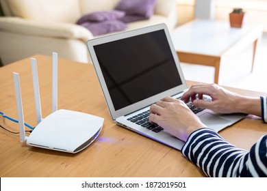 Selective Focus At Men Hand While Type On Computer Laptop Keyboard While Using Internet. In Front Of High Speed Wireless Internet Router That Provide Wi-fi Signal Inside Of The House. 
