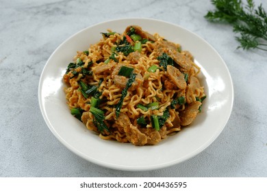 Selective focus Mie Goreng Tek-tek or fried noodles with topping slice meatballs, eggs and mustard greens (caisim or sawi hijau). Served in white plate. Look like noised with fried noodles. 