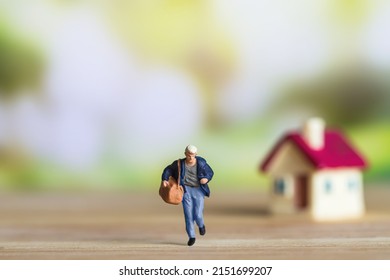 selective focus of miniature man  with tiny home model  on wooden floor over blurred bokeh background