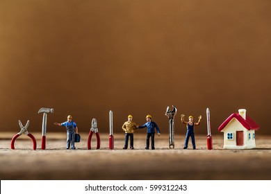 selective focus of miniature worker working with tool tools supplies and tiny home model  on wooden floor,macro photography concept idea for solution of property management service.