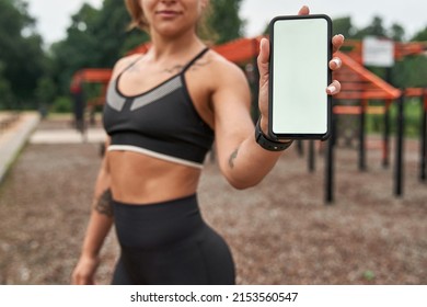 Selective focus of mobile phone in hand of blurred sportswoman on sports ground. Slim adult woman with tattoos wearing sportswear. Concept of modern female healthy and sports lifestyle