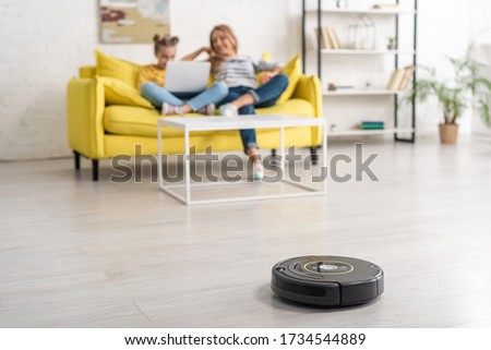 Selective focus of mother and daughter with laptop on sofa near coffee table and robotic vacuum cleaner on floor in living room Stock photo © 