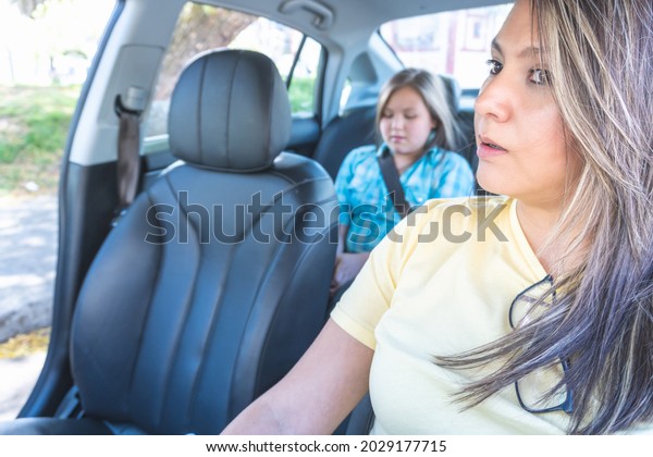 Selective focus of a mother driving her\
car with her daughter in the back seat with a\
belt