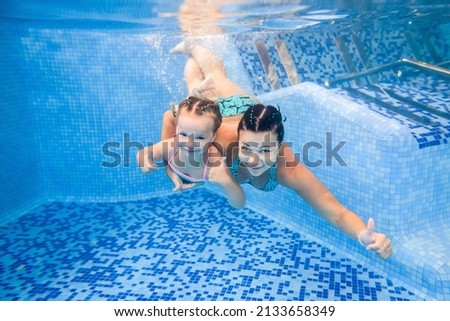 Selective focus. Mother holds daughter, submerged under water, swimming underwater in paddling pool. Diving baby. Learning infant girl to swim. Teaches infant child to swim.