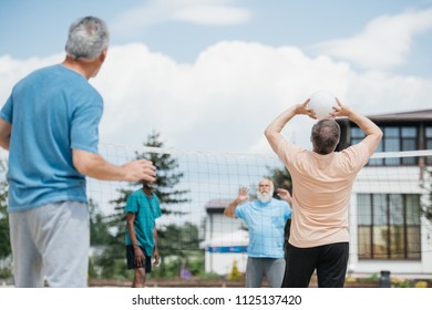 Selective Focus Of Multicultural Old Friends Playing Volleyball On Beach On Summer Day