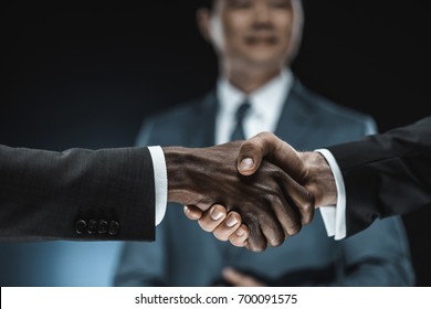 selective focus of multiethnic business partners shaking hands with colleague standing near by