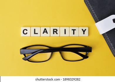 Selective focus with noise effect of notebook, eyeglasses and scrabble alphabets with text CLARITY over yellow background
