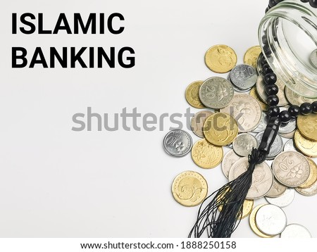 Selective focus with noise effect phrase ISLAMIC BANKING with coins spilled from a glass jar and rosary isolated on white background.Islamic finance concept.