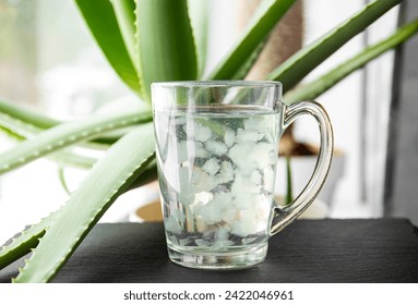 Selective focus on aloe vera juice drink with fruit flesh pieces floating inside. Healthy homemade drink with aloe vera plant growing on the background.  - Powered by Shutterstock