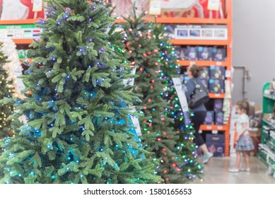 Selective Focus On Artificial Christmas Tree With Pre-lit Multi Color Lights And Defocused Customer Shopping In Background. Holiday Decoration At Home Improvement Store In Texas, America