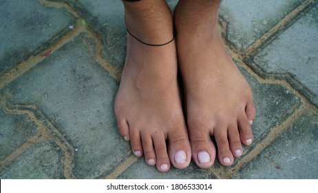 Selective focus on Bare feet of a little girl wearing black thread as anklet, standing on floor. Indian traditional culture concept.