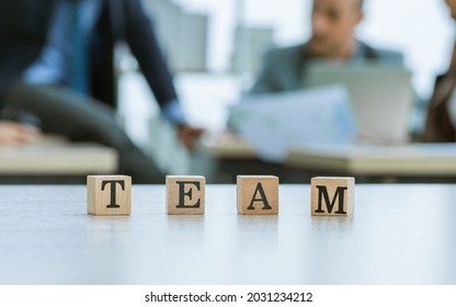 Selective Focus On Block Letters Of TEAM To Present Or Show About Teamwork, Collaboration And Unity With Blur Background Of Staff Success Working Together In Indoor Modern Office