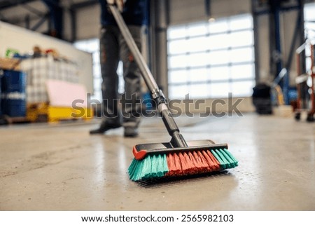 Selective focus on a broom dusting facility floor.