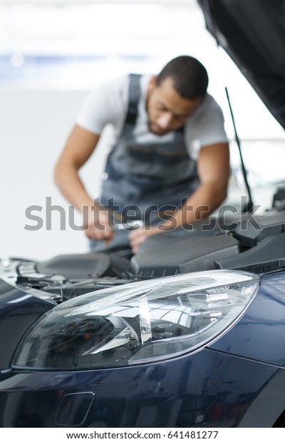 Selective focus on a car with the hood open\
professional mechanic repairing car engine on the background\
copyspace profession occupation vehicle auto repair service garage\
workshop technology\
concept