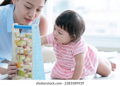 Selective focus on Caucasian cute 7 months daughter toddler baby face playing with alphabet blocks toy, sitting on floor with young Asian mother at home. Development, education, growth child care - Powered by Shutterstock