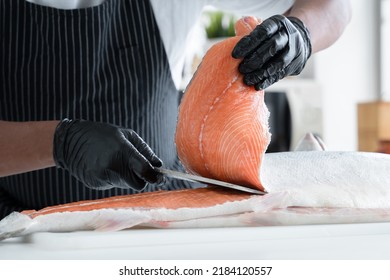 Selective focus on chef man hand, with black glove holding fresh salmon while another hand holding knife skillfully to cut salmon at kitchen. Anonymous chef prepare raw ingredients for Japanese food - Powered by Shutterstock